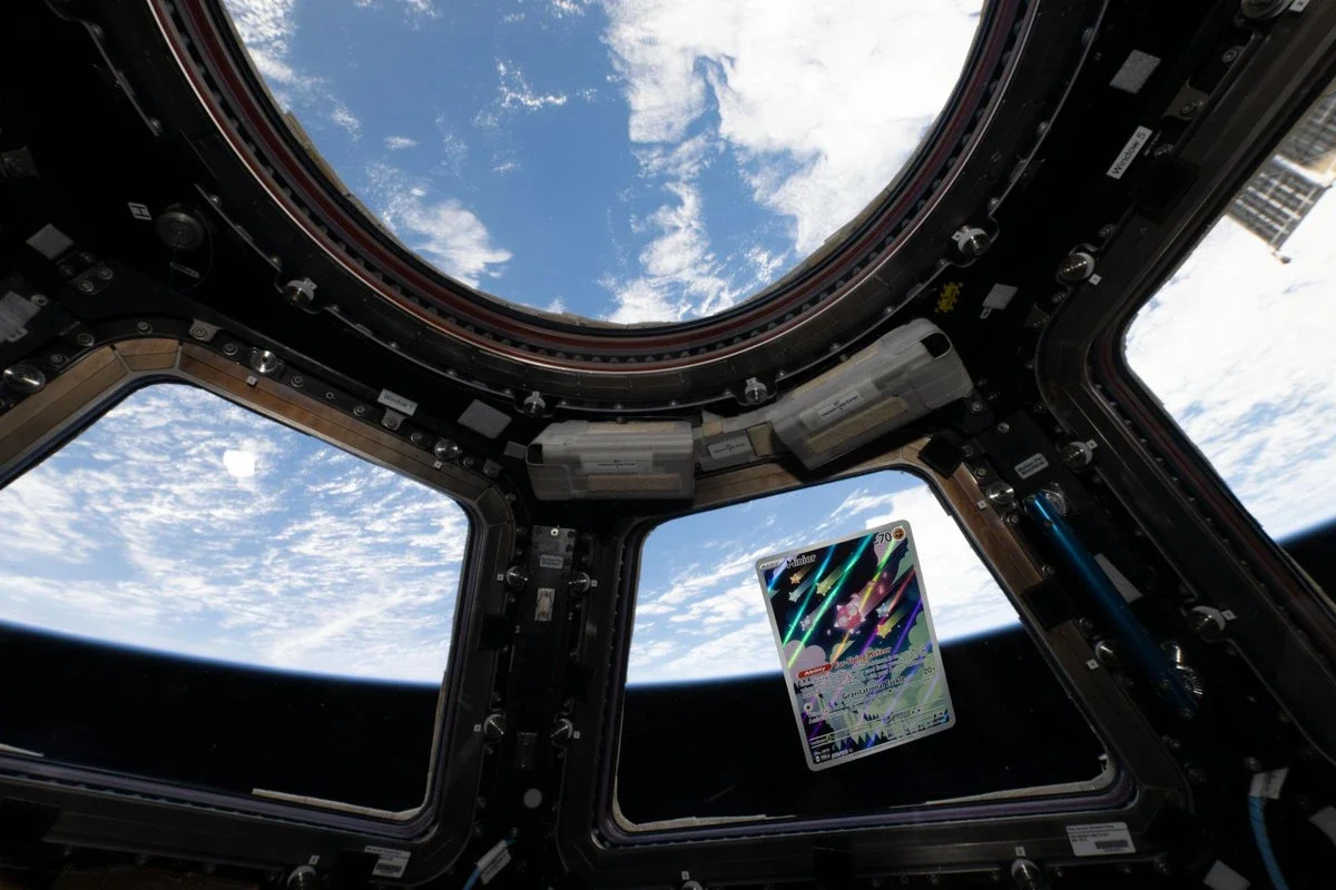 Minior Pokémon card floating in front of a window in the ISS Cupola, with Earth and clouds outside